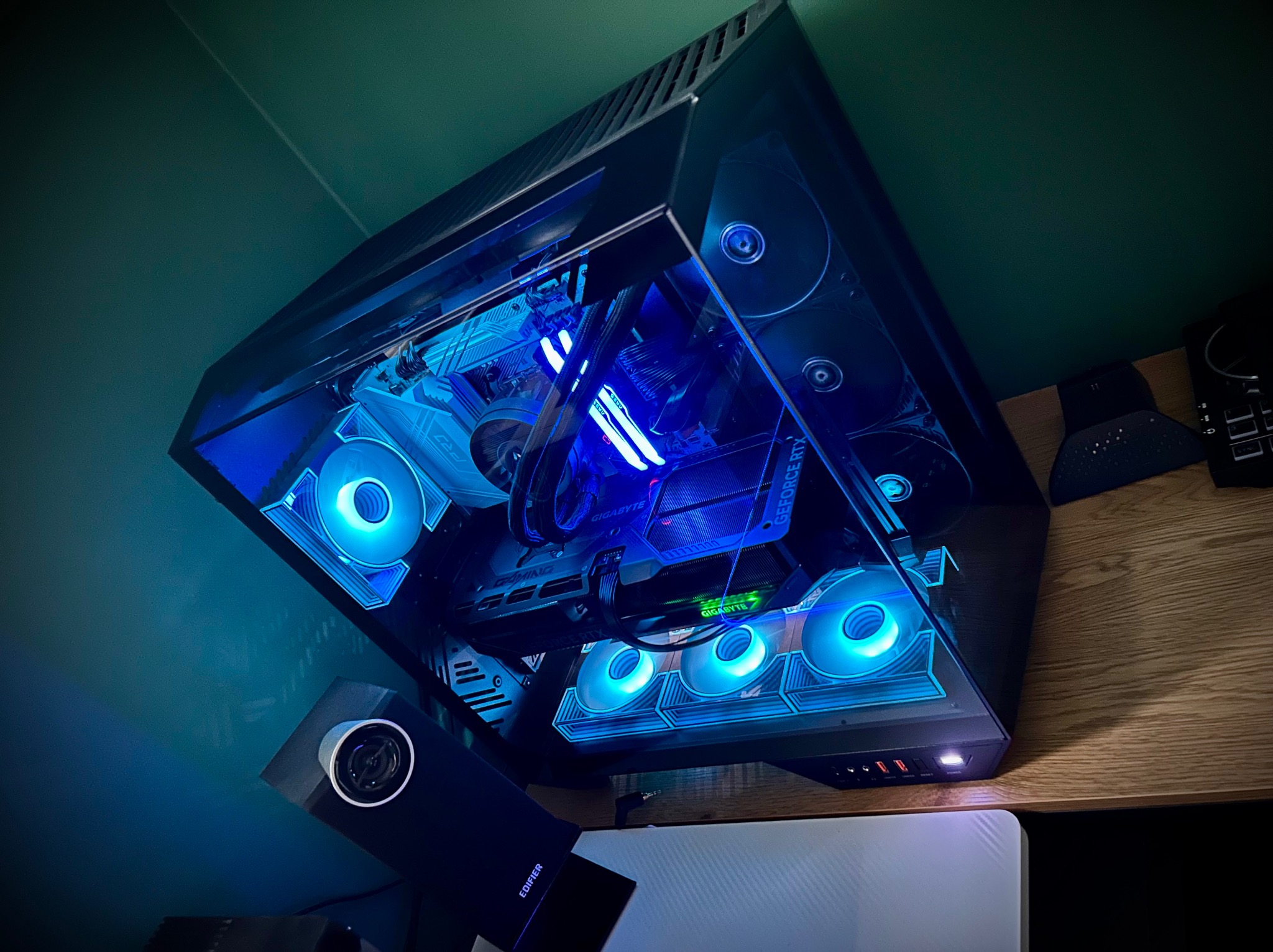 Komputer stacjonarny z podświetleniem LED w obudowie z oknem, widoczne komponenty: karta graficzna Gigabyte, chłodzenie. Obudowa stoi na drewnianym blacie.