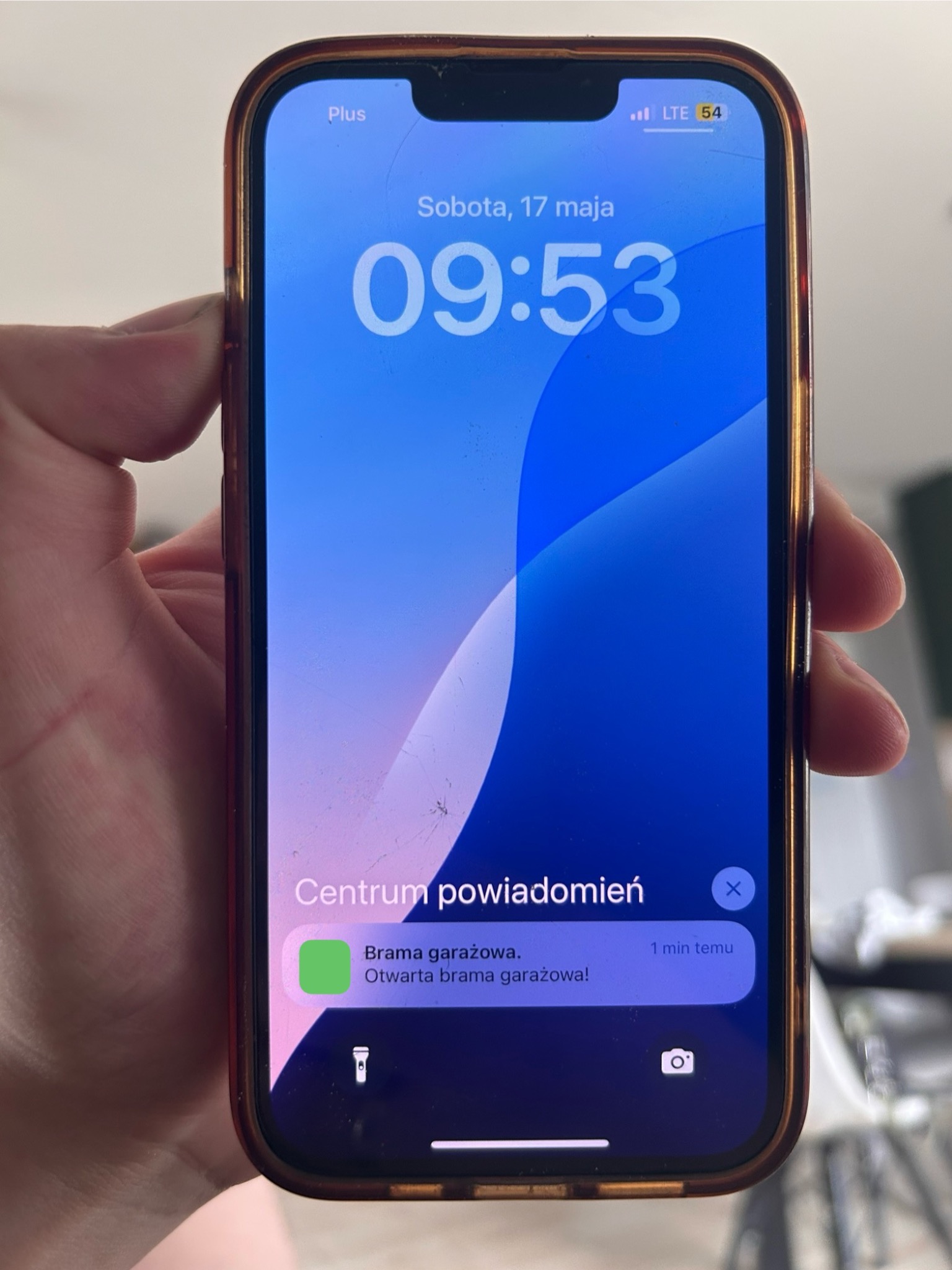 Smartfon w dłoni wyświetla powiadomienie o otwartej bramie garażowej. Aplikacja do zdalnego sterowania bramą. Zabezpieczenia domu i kontrola dostępu.