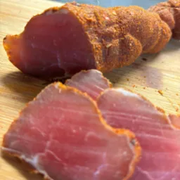 Krojony, wędzony schab obtoczony w przyprawach, ułożony na drewnianej desce. Widoczne grube plastry mięsa o intensywnym różowym kolorze.