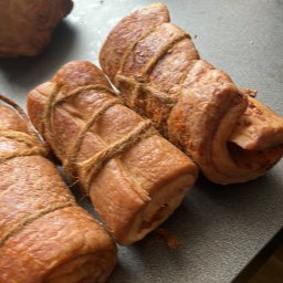 MICADO ELIZA MARIA WĘCOWSKA RESTAURACJA PEŁEN GARNEK - Wędliny wędzone, zawinięte sznurkiem, ułożone na szarym blacie, z widoczną fakturą powierzchni.