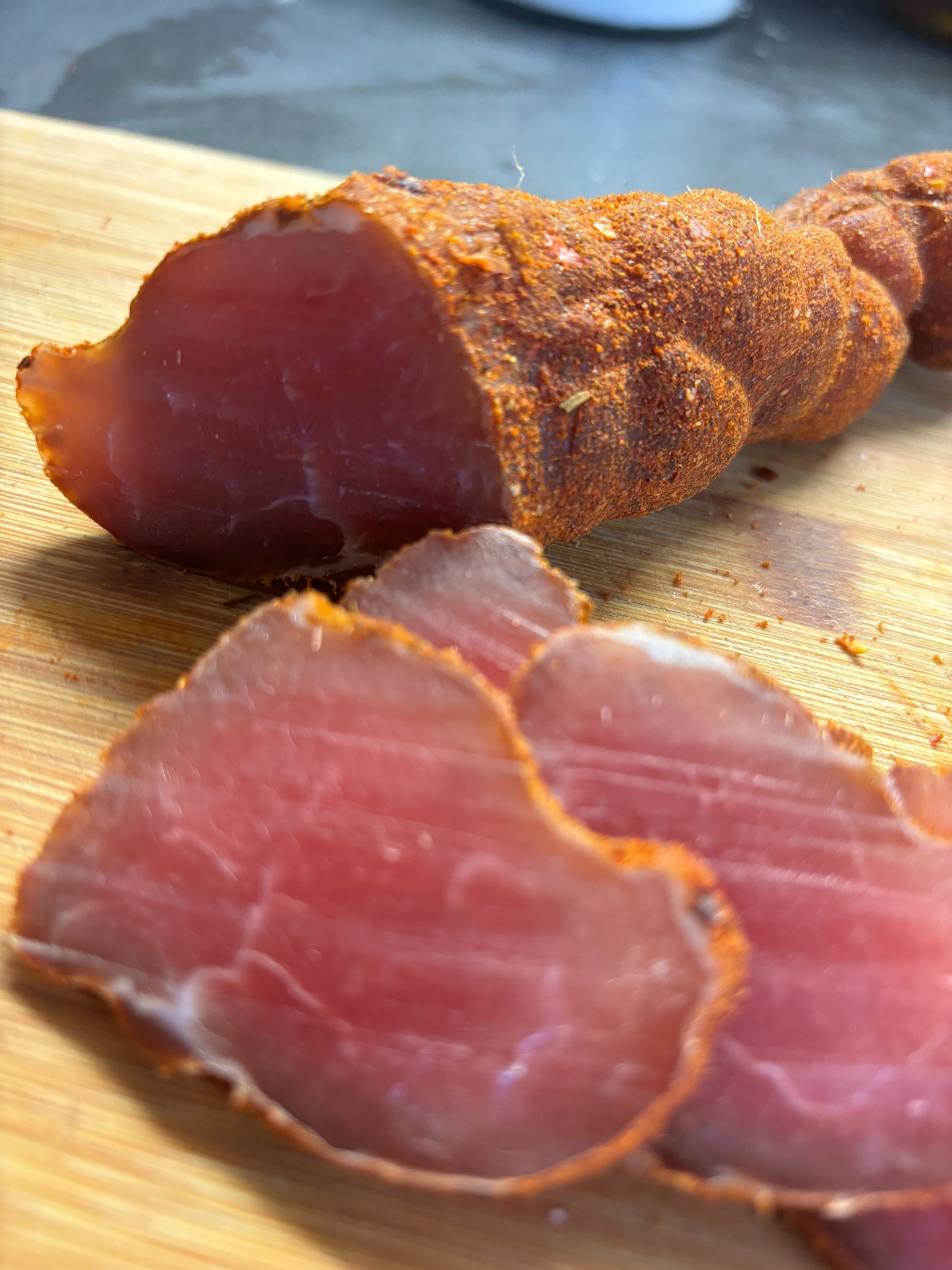 Krojony, wędzony schab obtoczony w przyprawach, ułożony na drewnianej desce. Widoczne grube plastry mięsa o intensywnym różowym kolorze.