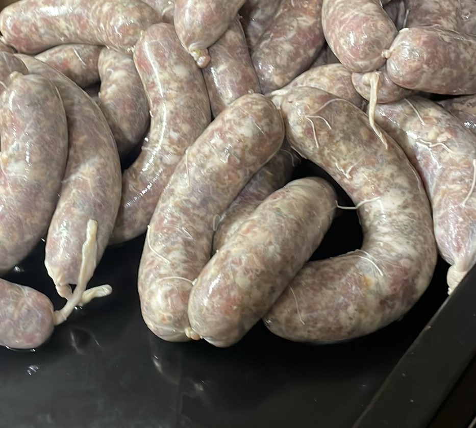 Kiełbasy w naturalnych osłonkach, ciasno ułożone na czarnej, błyszczącej powierzchni, związane sznurkiem.