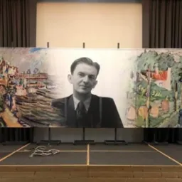 Scena z mównicą i dużym banerem przedstawiającym czarno-biały portret mężczyzny na tle abstrakcyjnego pejzażu miejskiego i wiejskiego.