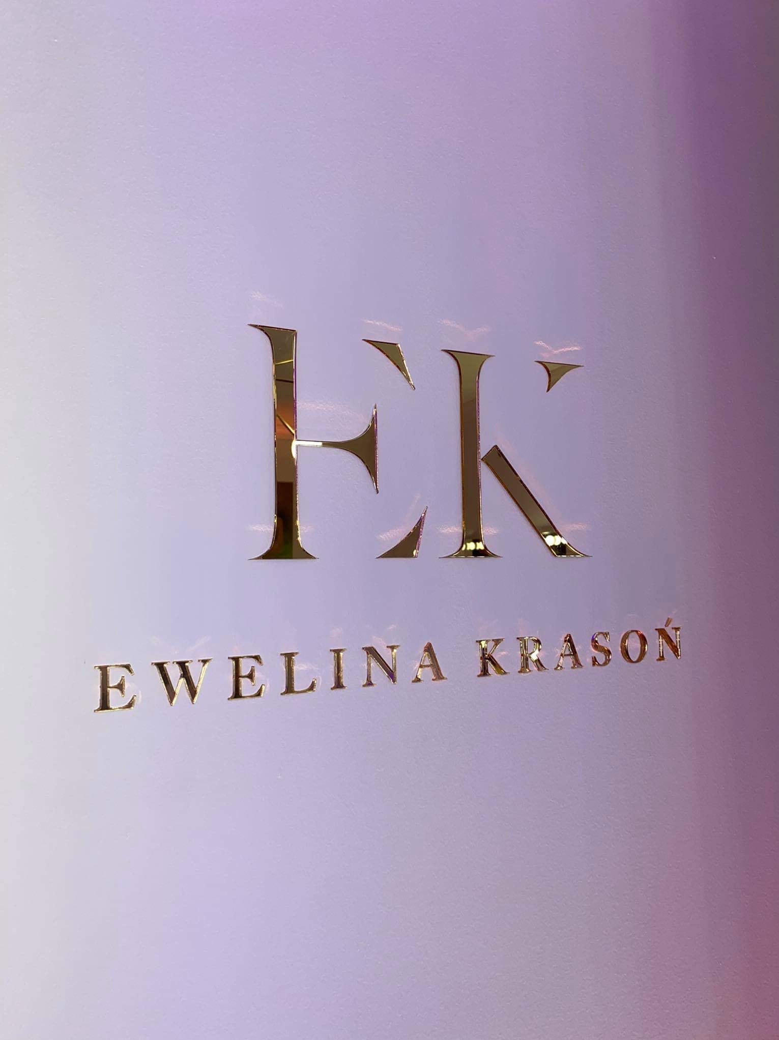 Złote litery 'EK' i napis 'Ewelina Krasoń' na jasnofioletowym tle, błyszczące logo.