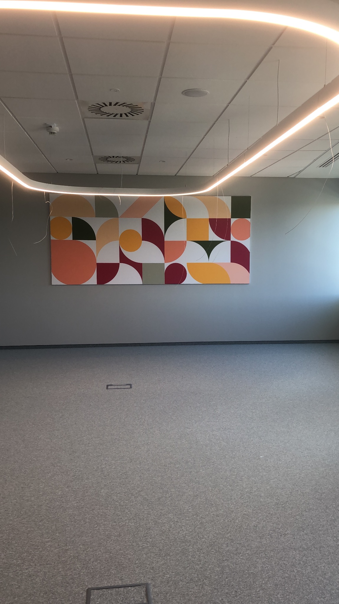 Wnętrze biura z abstrakcyjnym obrazem geometrycznym na ścianie, oświetlonym przez nowoczesną lampę LED