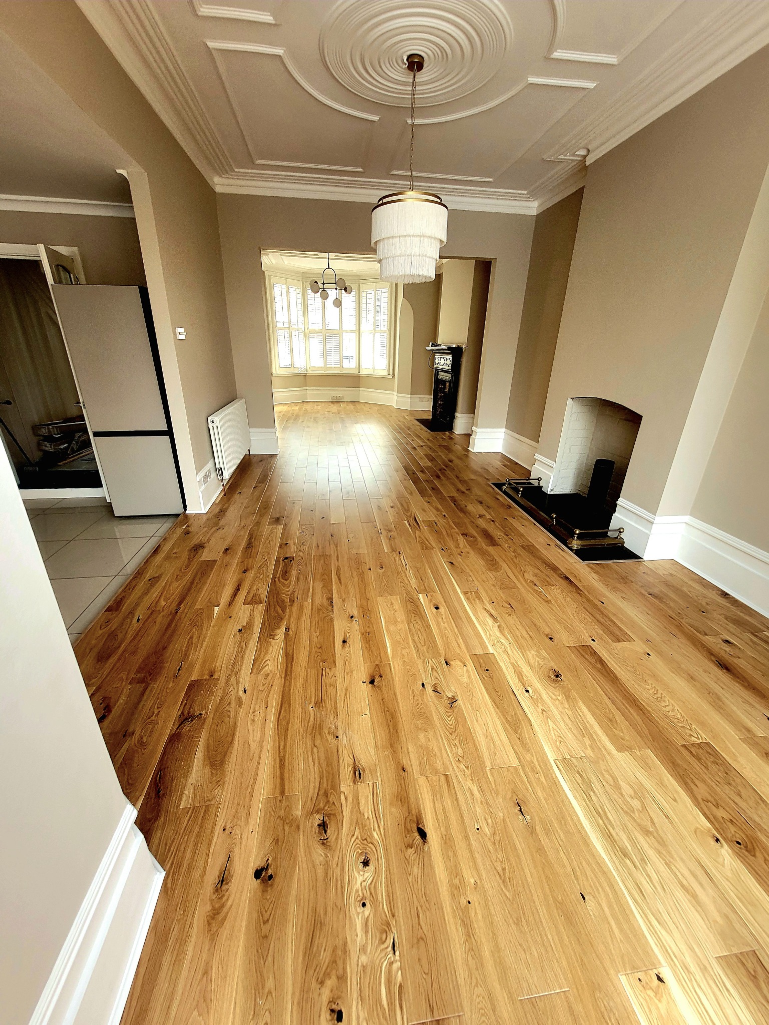 Salon po remoncie z ułożonym parkietem z naturalnego drewna, widoczny kominek i dekoracyjna lampa wisząca.