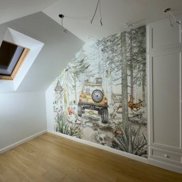 Pro-Bud Krzysztof Kargut - Pokój na poddaszu z drewnianą podłogą i fototapetą przedstawiającą leśny krajobraz z samochodem terenowym, widoczne niedokończone instalacje elektryczne na suficie.