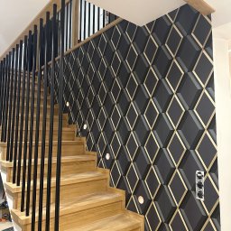 Pro-Bud Krzysztof Kargut - Nowoczesne schody drewniane z czarną balustradą i ścianą pokrytą tapetą 3D w geometryczne wzory z elementami złota, oświetlenie punktowe w ścianie.