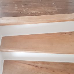 Pro-Bud Krzysztof Kargut - Schody drewniane z jasnego drewna, białe podstopnice, widoczny fragment podłogi z ciemniejszego drewna z widocznymi śladami zużycia.