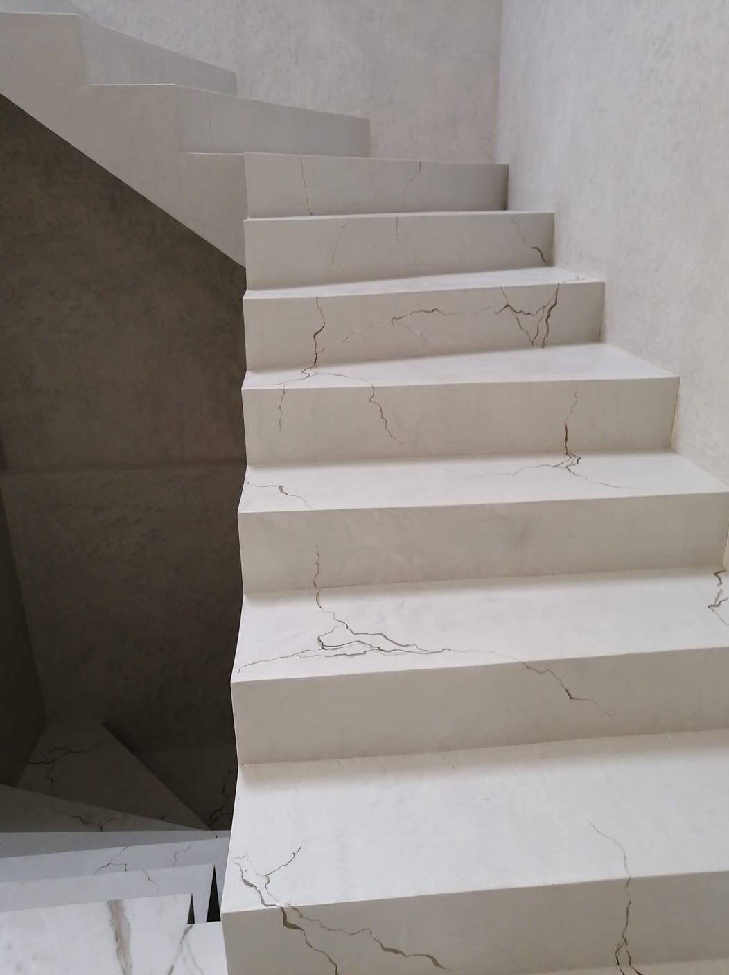 Schody wewnętrzne wykończone w jasnym odcieniu z efektem spękań, widoczne detale tekstury na stopniach i ścianie.
