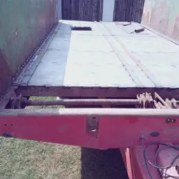 Metalowa platforma przyczepy w trakcie naprawy, z widocznymi nowymi spawami łączącymi blachy, oraz śladami rdzy na elementach konstrukcyjnych.