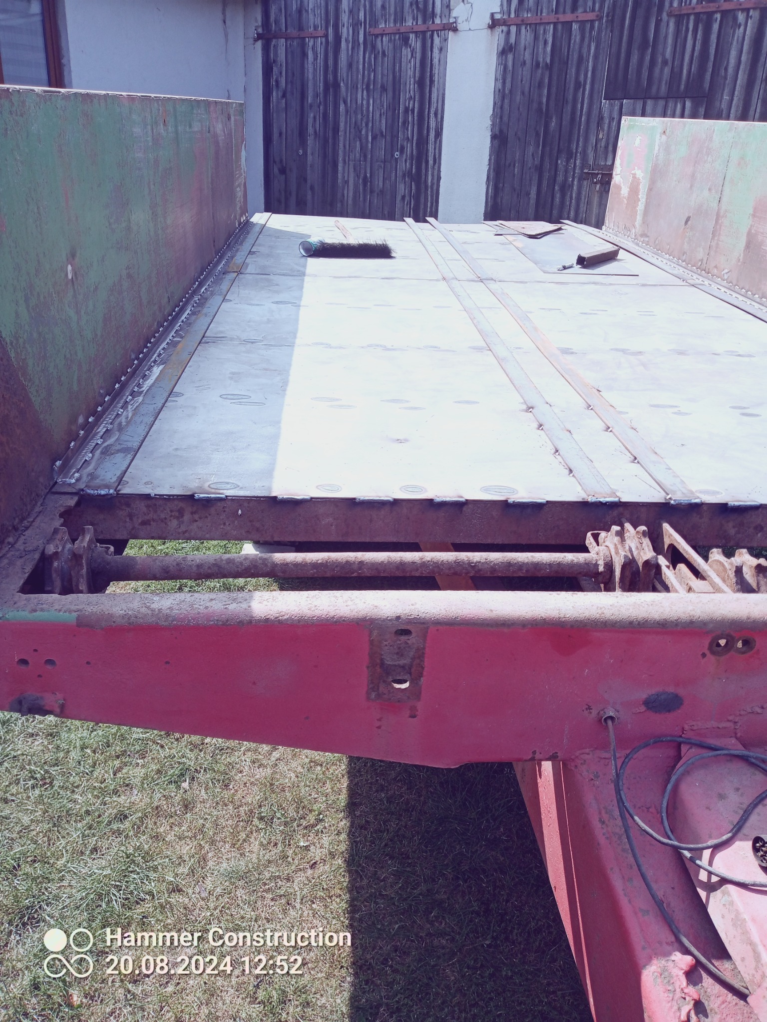 Metalowa platforma przyczepy w trakcie naprawy, z widocznymi nowymi spawami łączącymi blachy, oraz śladami rdzy na elementach konstrukcyjnych.