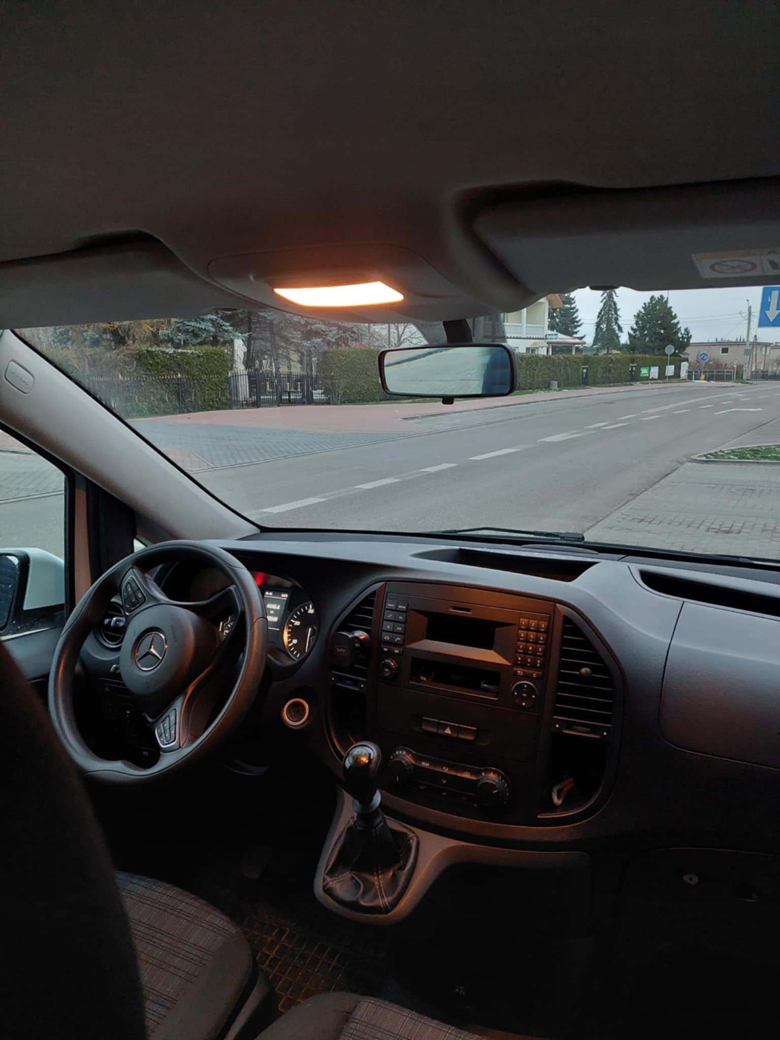 Wnętrze samochodu Mercedes Vito z widokiem na ulicę, deska rozdzielcza z radiem i klimatyzacją, kierownica z logo Mercedes-Benz, dźwignia zmiany biegów.