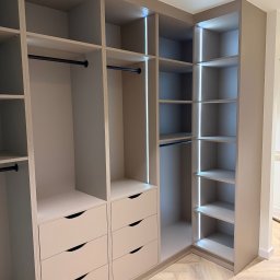 LUK-MEB Meble na wymiar - Jasna, narożna szafa wnękowa z szufladami i oświetleniem LED, widok z bliska na półki i drążki na ubrania. Parkiet w jodełkę na podłodze.