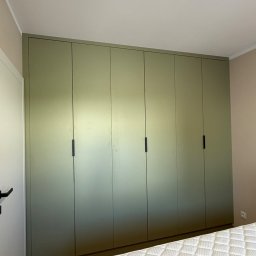 LUK-MEB Meble na wymiar - Szafa wnękowa z sześcioma drzwiami w odcieniach zieleni, z minimalistycznymi, czarnymi uchwytami, dopasowana do ściany w sypialni. Widoczny fragment łóżka.