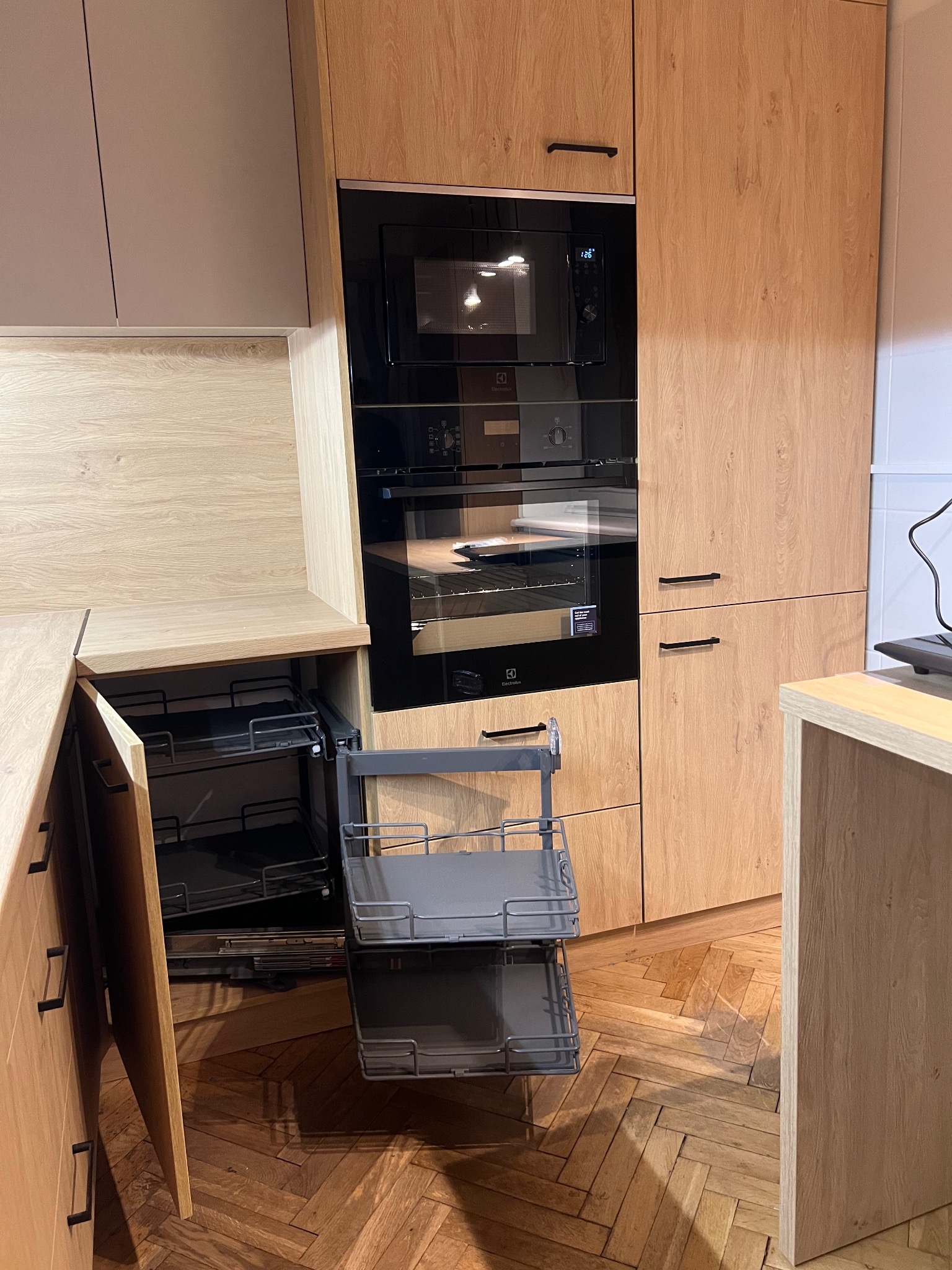 Drewniana zabudowa kuchenna z wysuwanymi koszami cargo i piekarnikiem w Kleczy Górnej. Fronty w odcieniach beżu i szarości, parkiet w jodełkę.