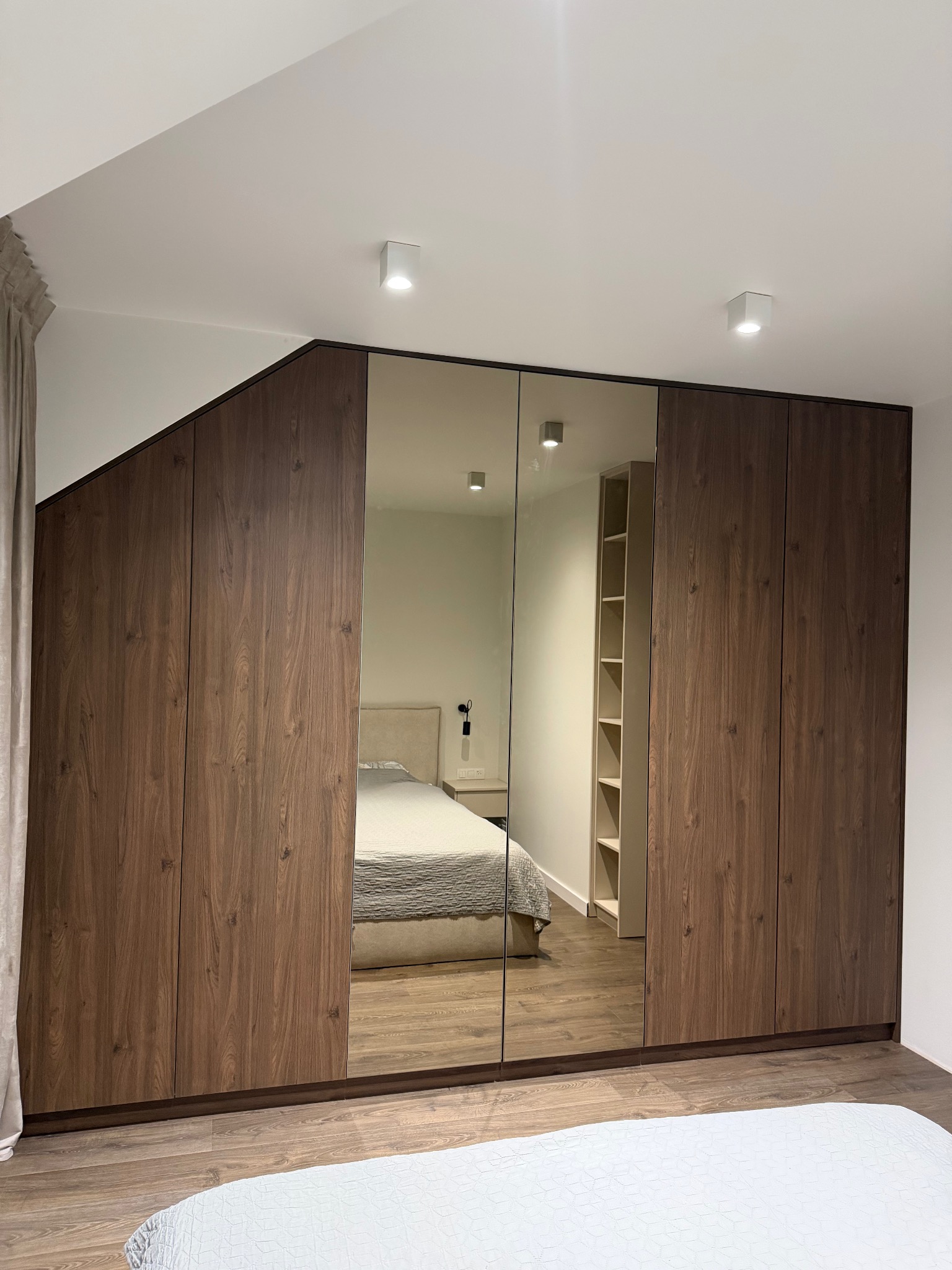 Duża szafa wnękowa z lustrzanymi drzwiami, drewnopodobne wykończenie, nietypowy kształt dopasowany do skosu sufitu, widok na sypialnię w Kleczy Górnej.