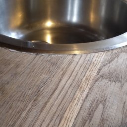 Vitalii Furman - Okrągły, metalowy zlew wpuszczony w blat z jasnego drewna o wyraźnym usłojeniu. Widoczne delikatne niedoskonałości wykończenia wokół zlewu.