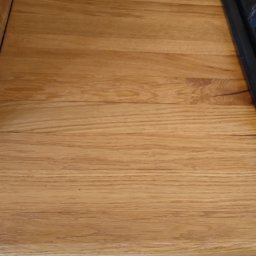 Vitalii Furman - Drewniany blat kuchenny z wbudowaną płytą grzewczą, widoczne słoje drewna i ozdobne wykończenie frontu szuflady. Ciepłe oświetlenie podkreśla naturalną barwę drewna.