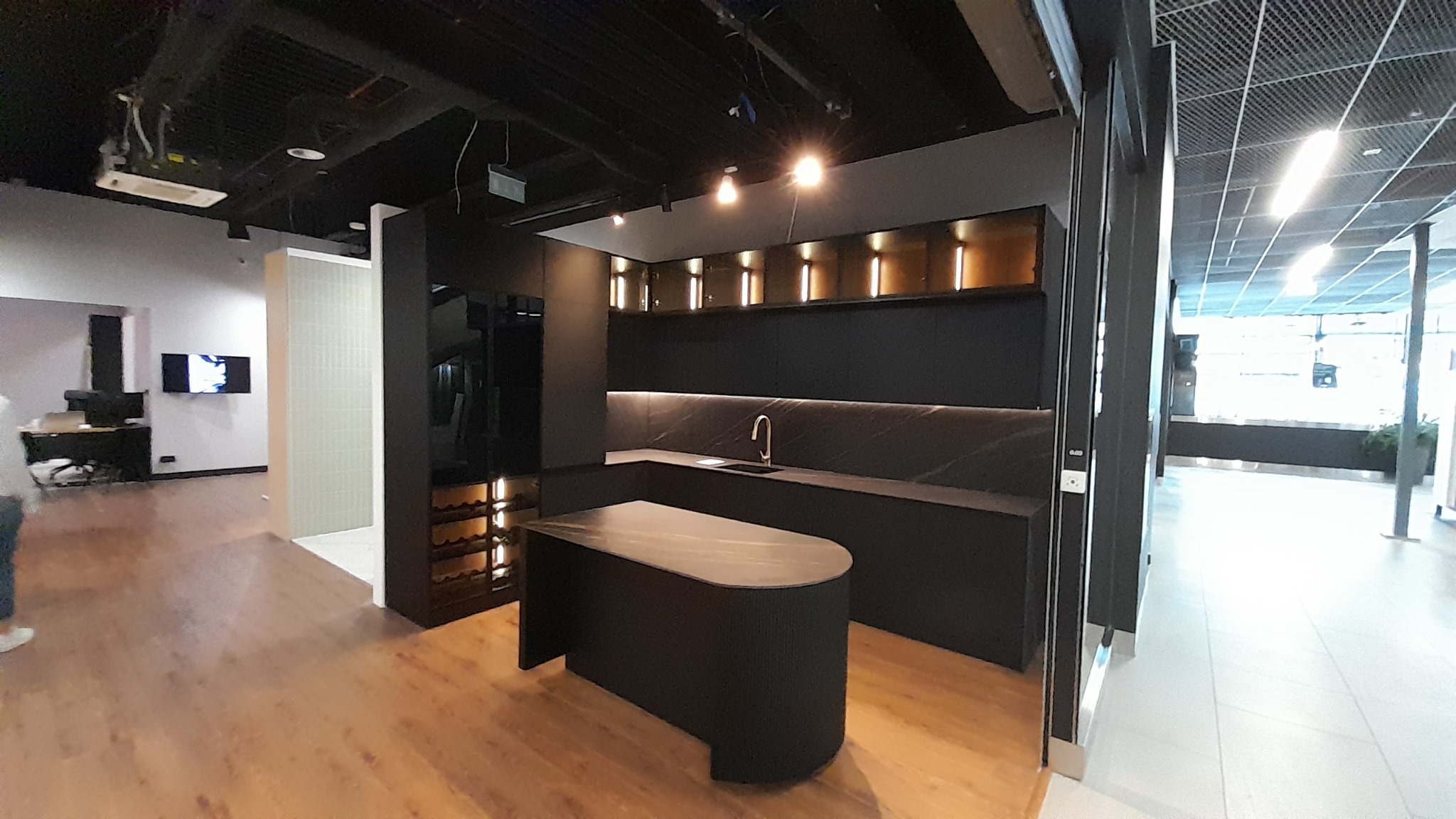 Nowoczesna, czarna kuchnia na wymiar z wyspą i oświetleniem LED. Widoczna zabudowa z szafkami górnymi i dolnymi, blat z ciemnego kamienia. Minimalistyczny design.