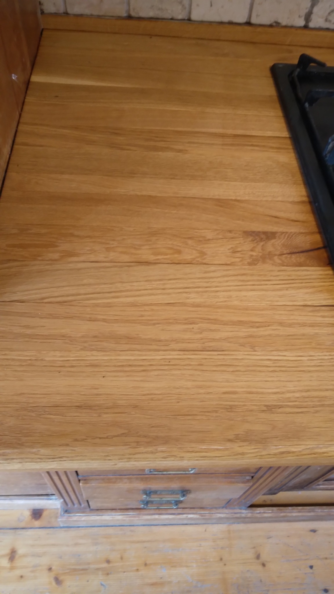 Drewniany blat kuchenny z wbudowaną płytą grzewczą, widoczne słoje drewna i ozdobne wykończenie frontu szuflady. Ciepłe oświetlenie podkreśla naturalną barwę drewna.