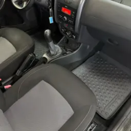 Wnętrze samochodu Dacia Duster, widoczne czarne i szare fotele z białymi przeszyciami, gumowe dywaniki z wytłoczonym wzorem, deska rozdzielcza z radiem i kluczykami w stacyjce, uchwyty na napoje.