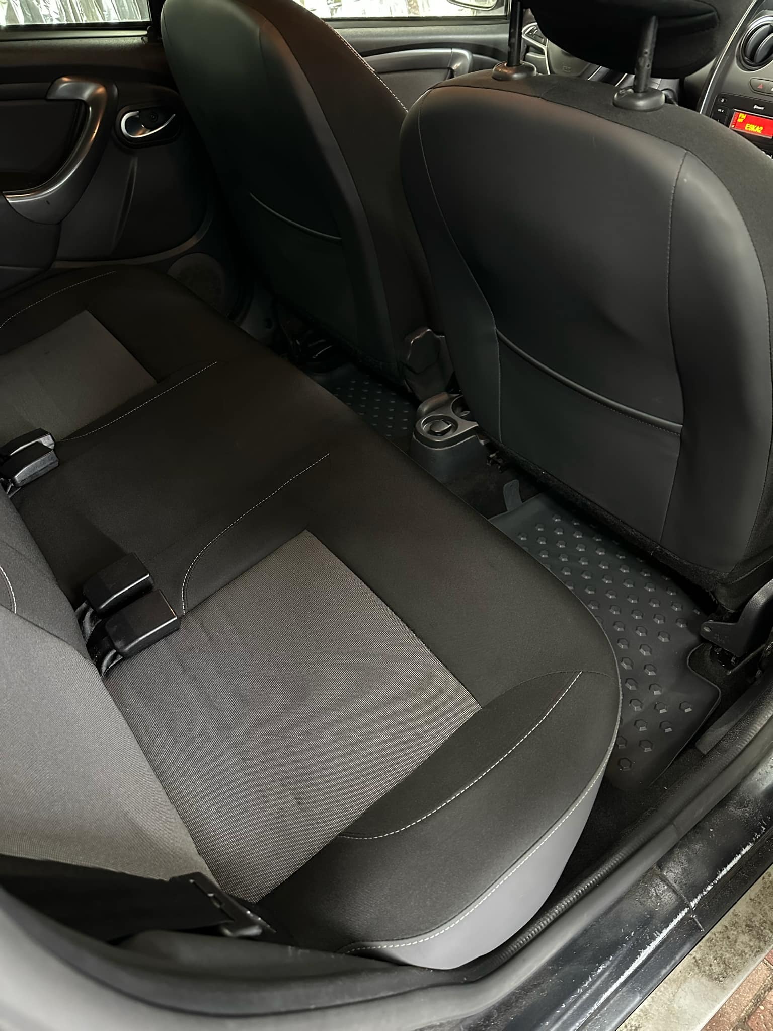 Wnętrze samochodu: tylna kanapa z czarno-szarą tapicerką i widocznymi pasami bezpieczeństwa, gumowe wycieraczki pod nogami