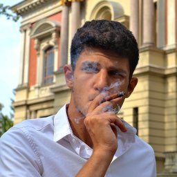 Uslugi fotograficzne - Mężczyzna w białej koszuli pali cygaro na tle klasycystycznego budynku z kolumnami. Dym otacza jego twarz, tworząc artystyczny efekt.