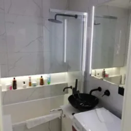 Nowoczesna łazienka z marmurowymi płytkami, czarną umywalką nablatową i oświetleniem LED w niszy nad wanną.