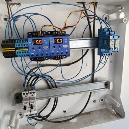 Elektro MP - Rozdzielnica elektryczna z zamontowanymi modułami, zabezpieczeniami i przewodami. Widoczne elementy sterujące i wyświetlacze. Instalacja wewnątrz białej obudowy.