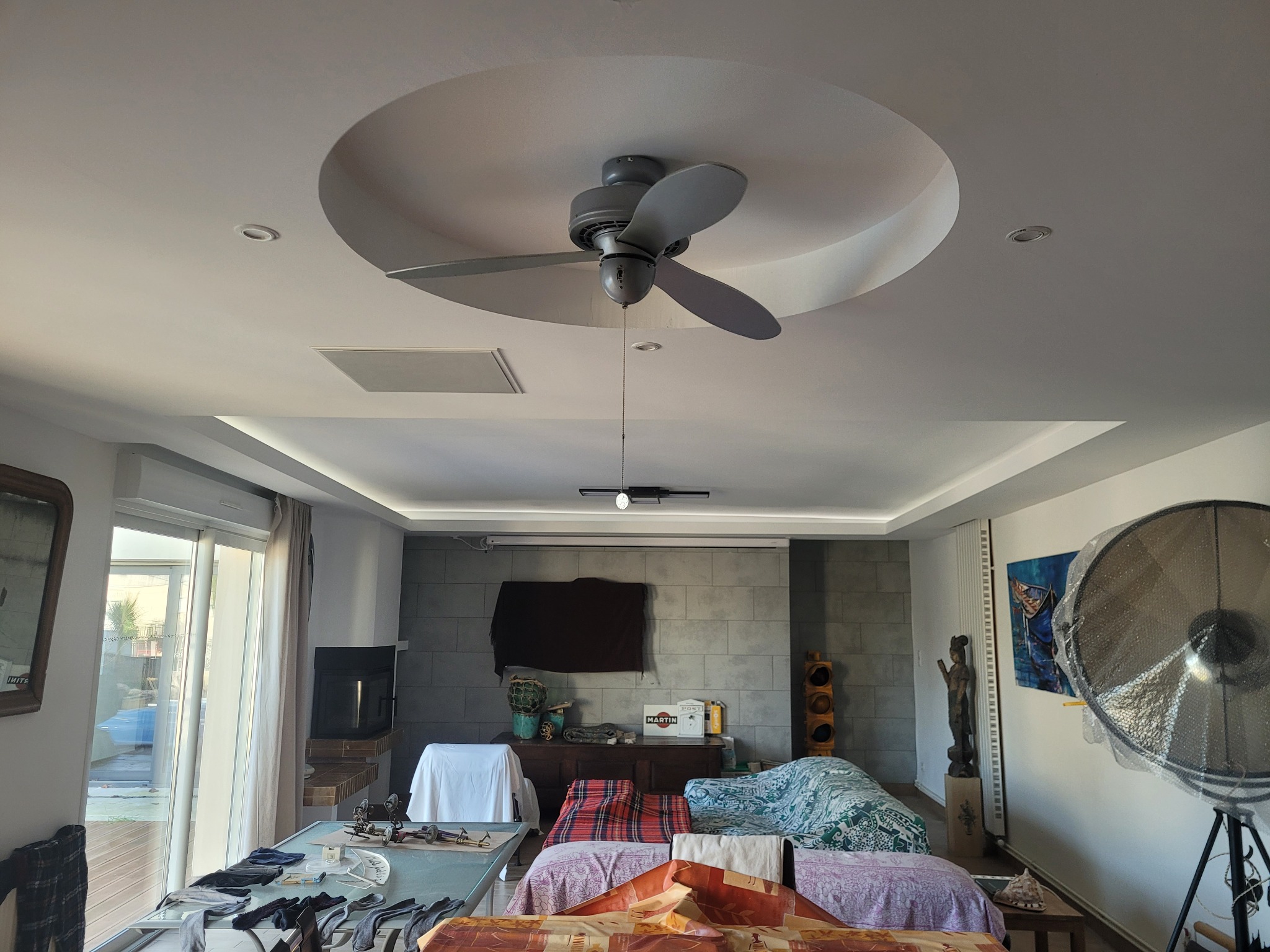 Wnętrze pokoju z szarą kolorystyką, oświetleniem LED w suficie podwieszanym, wentylatorem sufitowym i dekoracyjną ścianą z szarej cegły.