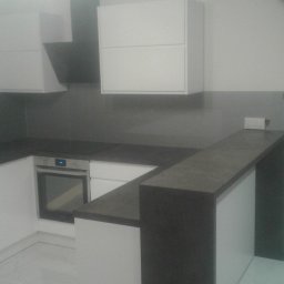 FRANCISZEK MIKOŁAJCZYK ZAKŁAD STOLARSKI - Nowoczesna kuchnia z białymi szafkami i ciemnym blatem, widok na piekarnik i okap, marmurowa podłoga.