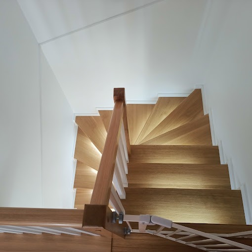 Nowoczesne, drewniane schody z podświetleniem LED w Limanowej, widziane z góry, z zamontowaną bramką zabezpieczającą dla dzieci.