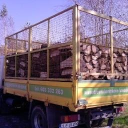Drewno kominkowe Lublin-Lubelskie - Żółta ciężarówka z metalową klatką załadowana pociętymi kawałkami drewna opałowego na pace, widoczny numer telefonu i adres strony internetowej na boku skrzyni.