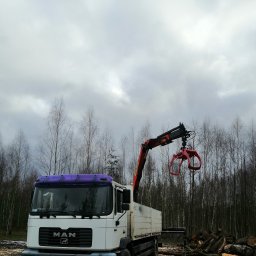 Drewno kominkowe Lublin-Lubelskie - Biała ciężarówka MAN z czerwonym żurawiem hydraulicznym do załadunku drewna na tle lasu z nagromadzonymi kłodami.