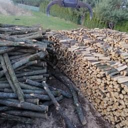 Stos drewna kominkowego w Cycowie: po lewej surowe gałęzie, po prawej pocięte i ułożone kawałki drewna, nad nimi chwytak do drewna.