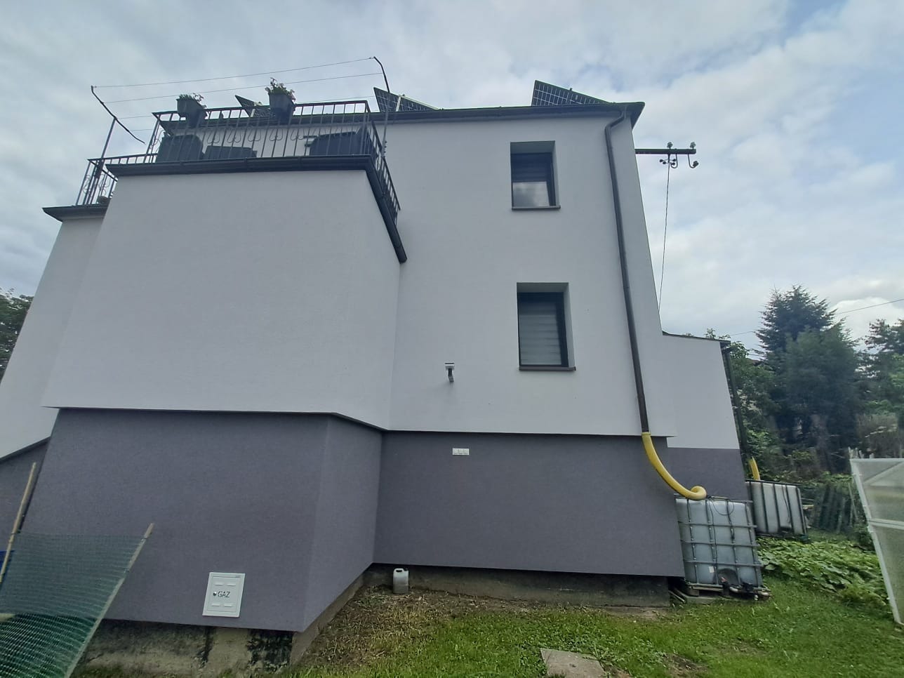 Elewacja domu po remoncie w Częstochowie z elementami instalacji odzysku wody deszczowej. Widoczne zbiorniki i rynna odprowadzająca wodę.