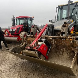 ARTEX Artur Rączka - Czerwony traktor z wałem ugniatającym i żółta ładowarka Volvo z ubijarką w łyżce, na żwirowym placu, operator w czarnej kurtce przy traktorze.