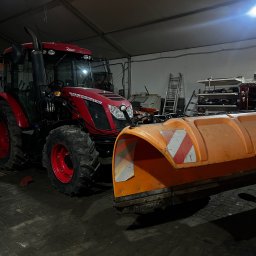 ARTEX Artur Rączka - Czerwony traktor Zetor z zamontowanym pomarańczowym pługiem śnieżnym w garażu, widoczne półki z narzędziami i drabina.