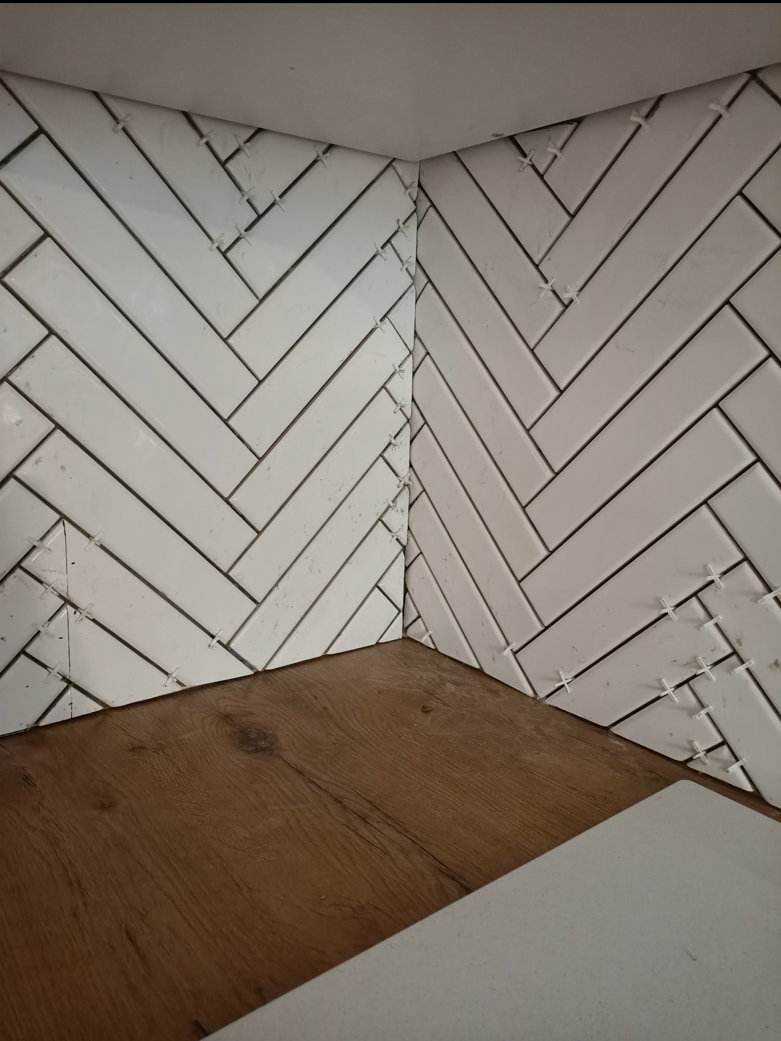 Układanie białych, prostokątnych płytek w jodełkę na ścianie w Stargardzie, widoczne krzyżyki dystansowe, dolna krawędź wykończona drewnopodobną listwą.
