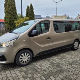 Beżowy van Renault Trafic z przyciemnianymi szybami, zaparkowany na kostce brukowej w miejskiej scenerii.