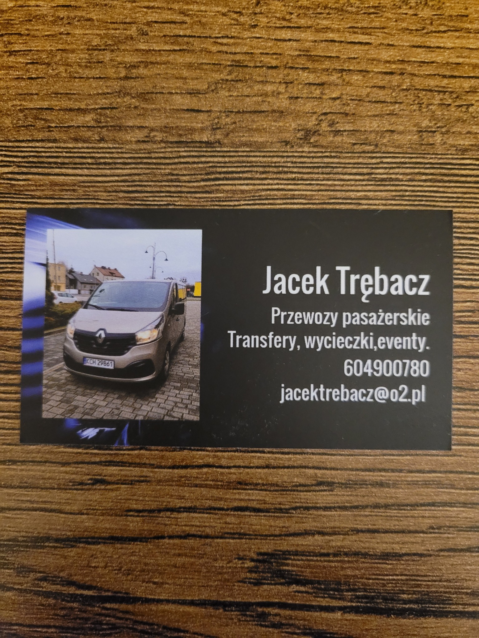 Wizytówka z szarą Renault Trafic na tle kostki brukowej, dane kontaktowe i nazwisko Jacek Trębacz.