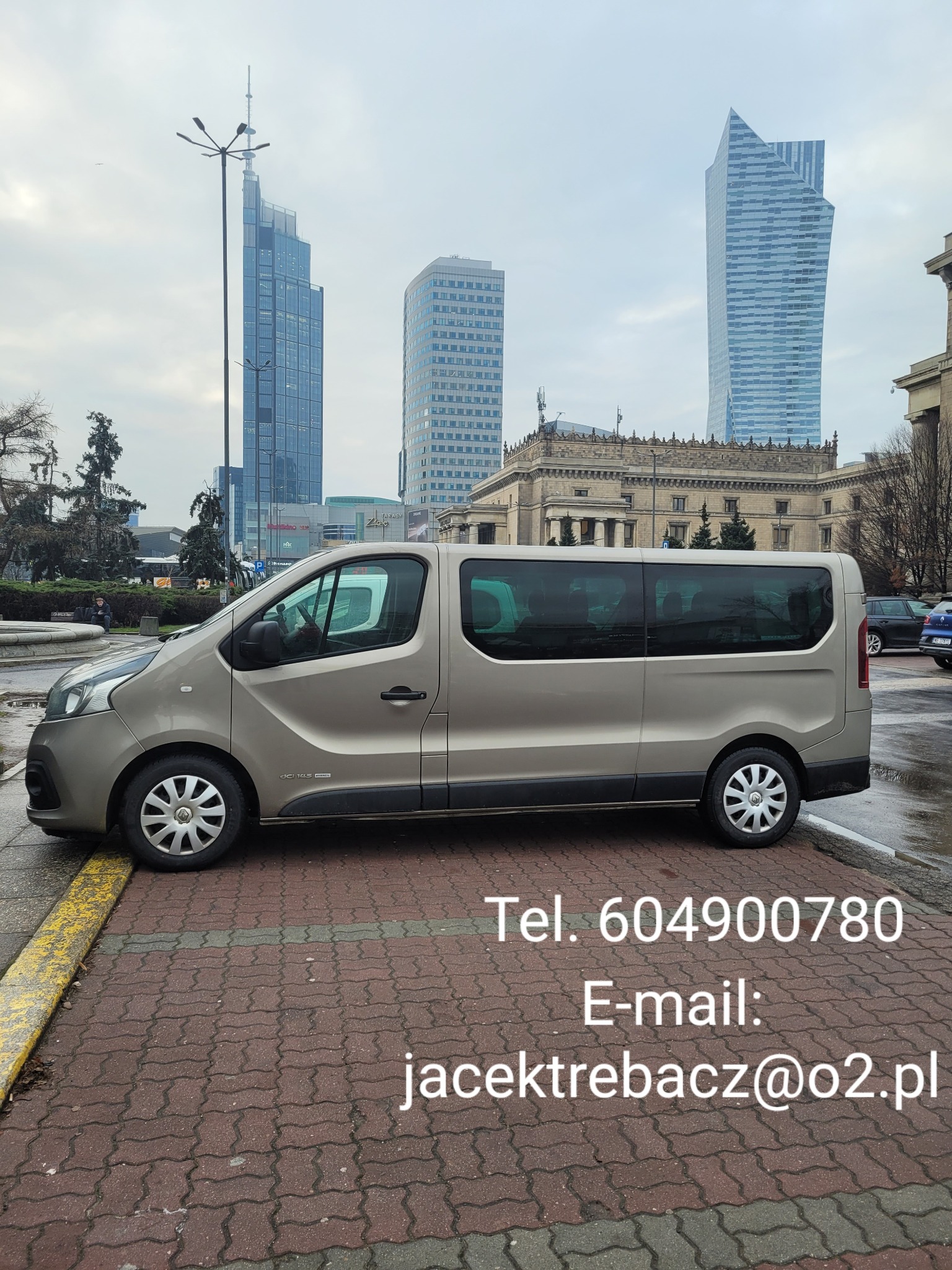 Beżowy van z widocznymi danymi kontaktowymi na tle warszawskiej architektury, w tym Pałacu Kultury i Nauki oraz nowoczesnych wieżowców.