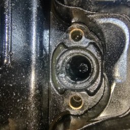 Firma Usługowa Sebastian Śmiech - Zbliżenie na fragment silnika samochodowego z widocznymi otworami montażowymi i śladami oleju, ukazujące detale konstrukcyjne i zużycie eksploatacyjne.