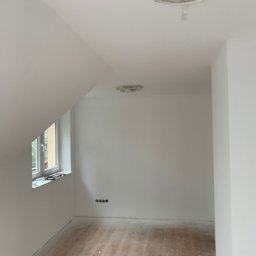 MJ GARDEN Marian Jarek - Poddasze po remoncie, świeżo pomalowane na biało, z drewnianą podłogą w trakcie czyszczenia, widoczne przygotowania do montażu oświetlenia sufitowego.