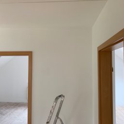 MJ GARDEN Marian Jarek - Świeżo pomalowane na biało ściany w mieszkaniu w Krakowie, widoczna drabina malarska, drewniana ościeżnica drzwi i fragment sufitu z listwą.