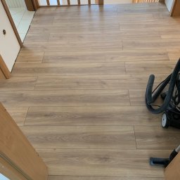 MJ GARDEN Marian Jarek - Ułożone panele podłogowe w korytarzu, widoczne przejście schodowe i odkurzacz, jasne drewno.