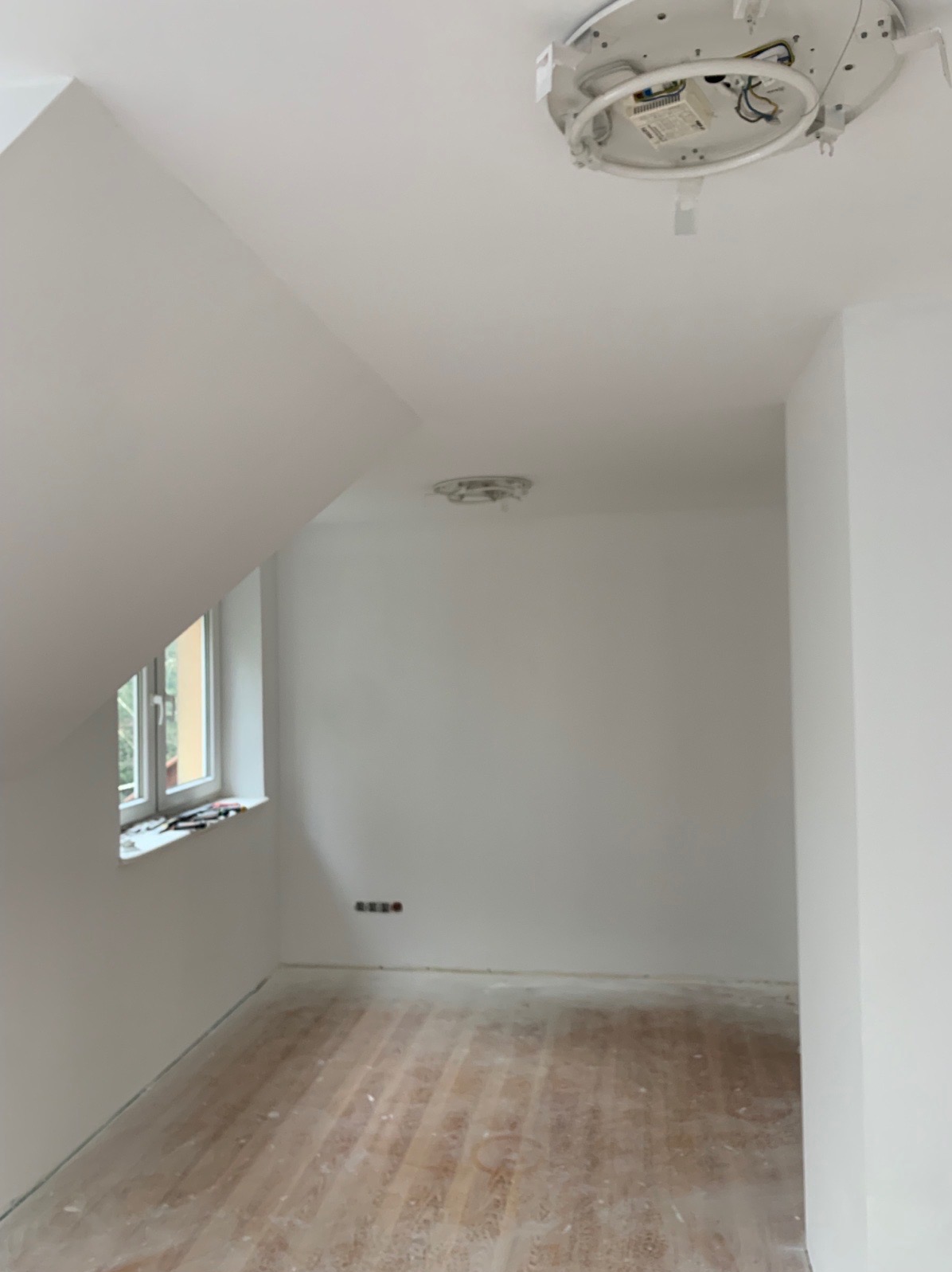 Poddasze po remoncie, świeżo pomalowane na biało, z drewnianą podłogą w trakcie czyszczenia, widoczne przygotowania do montażu oświetlenia sufitowego.