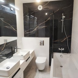 Tantum Optima - Nowoczesna łazienka z czarnymi płytkami imitującymi marmur z złotymi żyłami, białą armaturą, dwiema umywalkami nablatowymi, wiszącą toaletą i kabiną prysznicową ze szklaną ścianką.