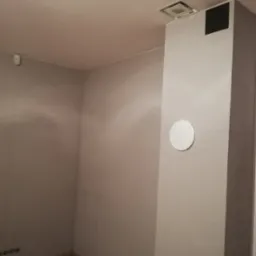 Wnętrze pokoju po malowaniu ścian na szaro, widoczny fragment podłogi z paneli, kolumna z otworem wentylacyjnym i kratką wentylacyjną na suficie.